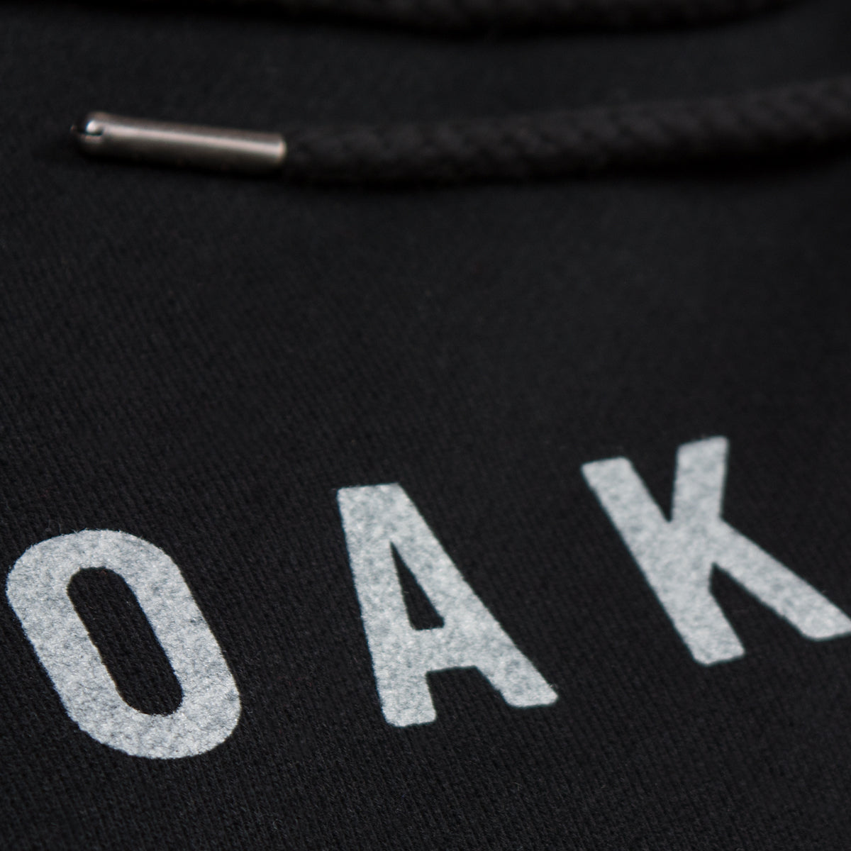 Close up of OAK in white capital letters on a black hoodie.