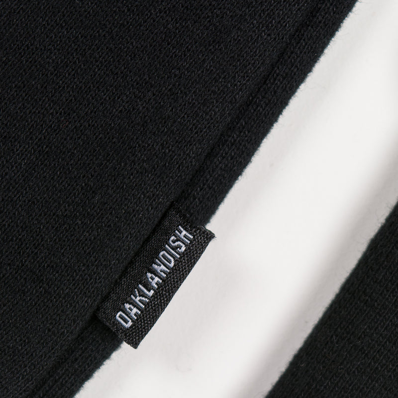 Close up of small Oaklandish wordmark tag on the side of a black hoodie.