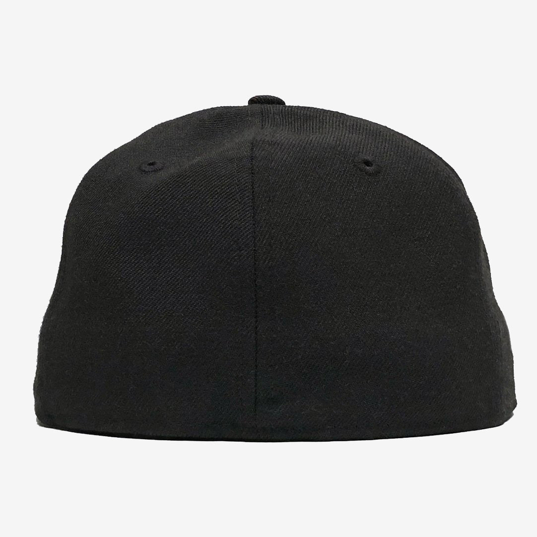 A plain black New Era OAK 59FIFTY Fitted Cap by Oaklandish seen from the back, showcasing a curved, seamless design. The cap has a slight texture and features two small ventilation holes on each side, totaling four. The background is plain white, and the cap's top button is centered and slightly visible.