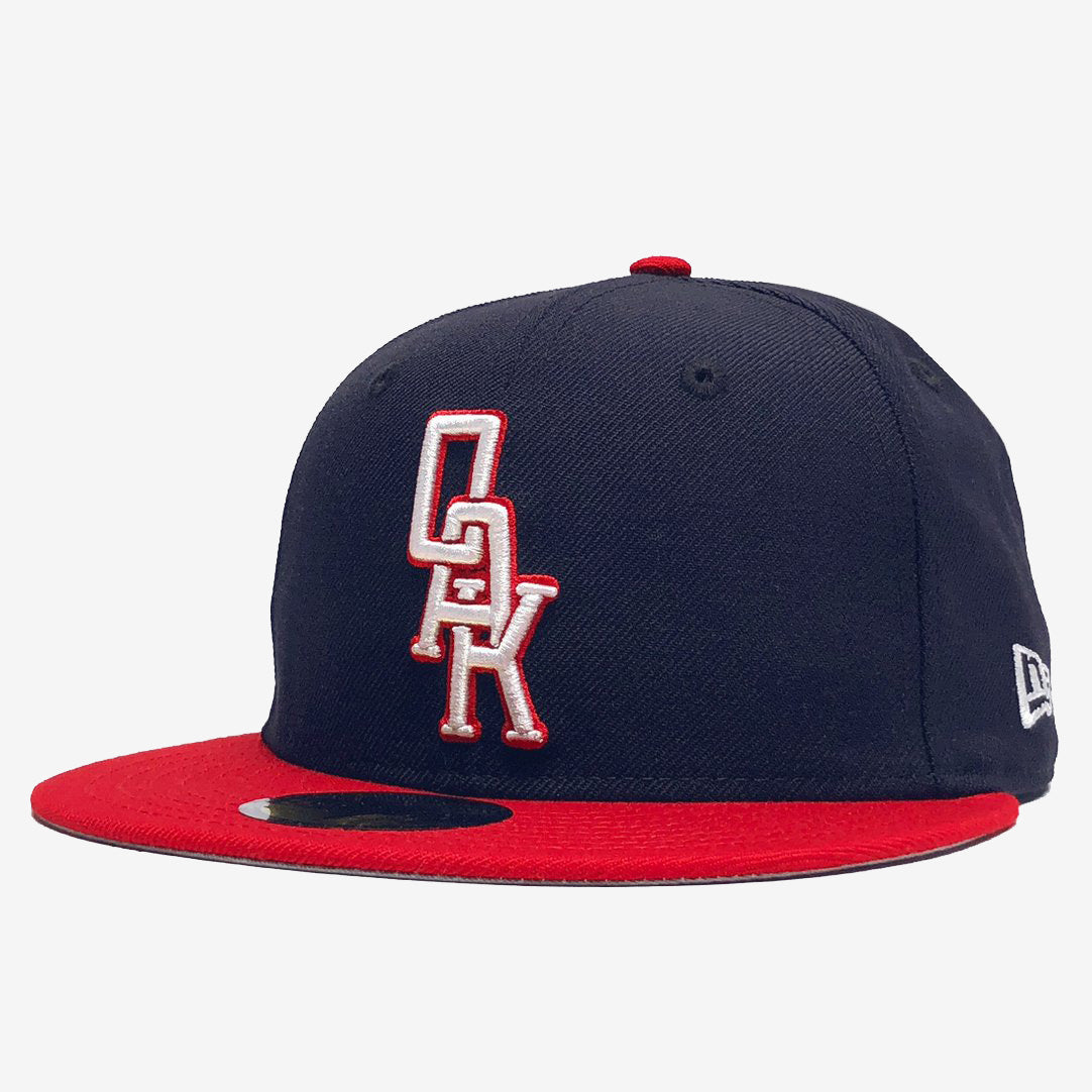 Navy New Era cap with red visor and white embroidered OAK wordmark on the crown.