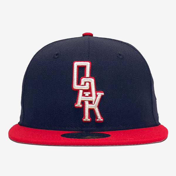 Navy New Era cap with red visor and white embroidered OAK wordmark on the crown.