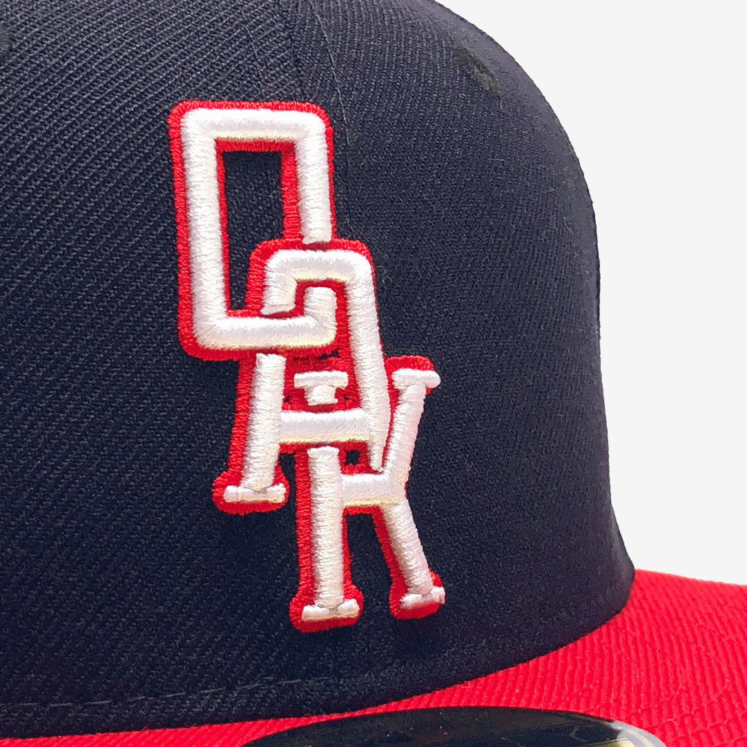 Close-up of a white embroidered OAK wordmark on the crown on a navy New Era cap.