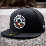 Black New Era cap with full-color circle Roots SC mosaic logo on the crown sitting on a sidewalk.