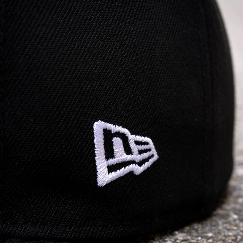 Close-up of white embroidered New Era logo on a black cap.