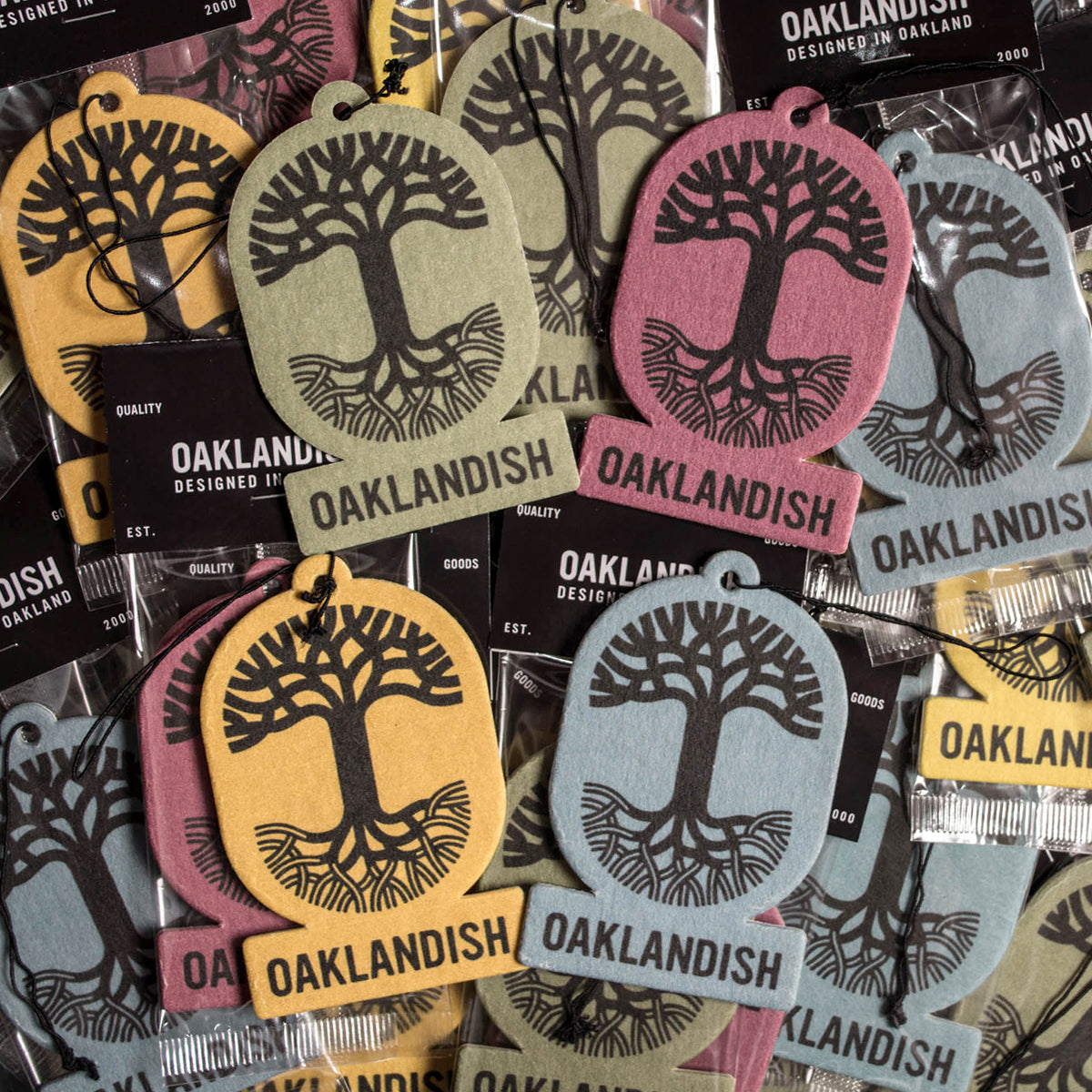 A collection of Oaklandish Air Fresheners by Oaklandish doubles as stylish accessories, each showcasing the iconic Oaklandish tree logo with "OAKLANDISH" displayed beneath it. The air fresheners are available in an array of colors including green, pink, yellow, and blue, and are individually wrapped in plastic packaging to ensure long-lasting scents.