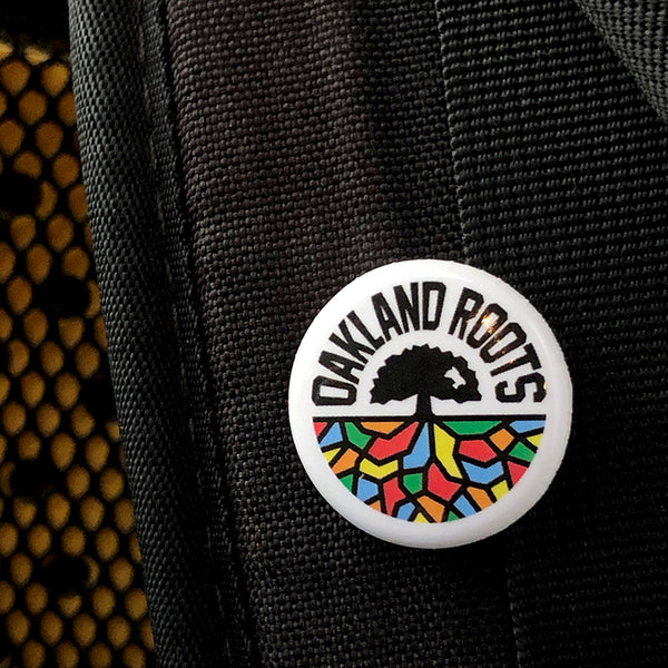 Oakland Roots full-color logo crest on a lapel pin, pinned to black canvas.