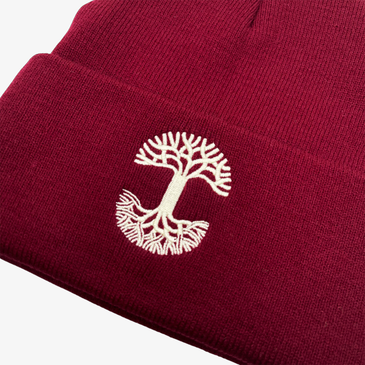 Close-up of white embroidered Oaklandish tree logo on the cuff of a burgundy beanie.