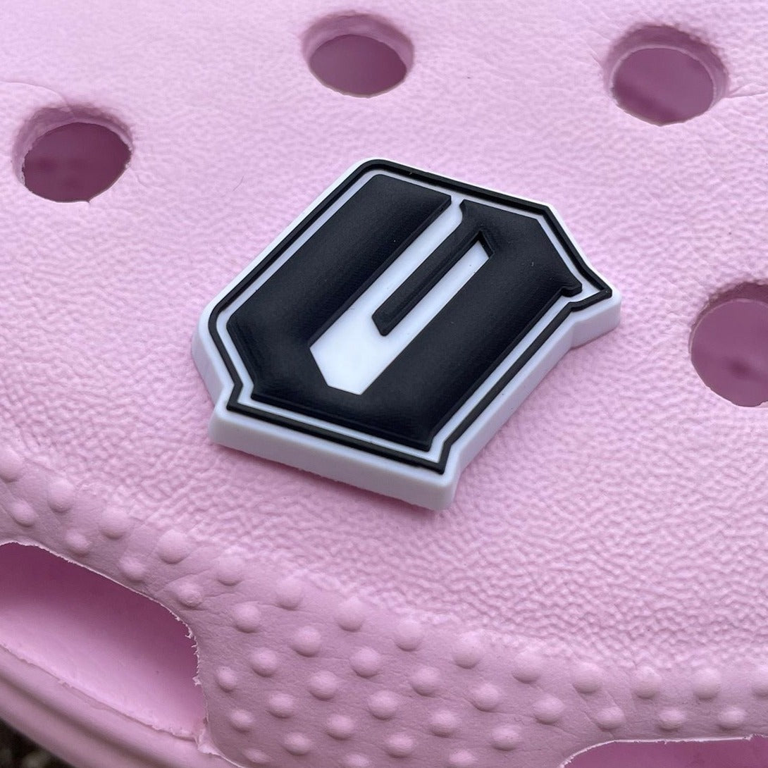 Black and white Oaklandish O logo shoe charm on a pink croc shoe.