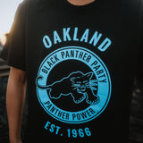 Close-up of a large blue Black Panther Power logo on the chest of a black t-shirt worn on female model.