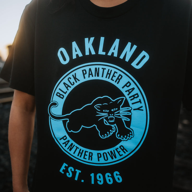 Close-up of a large blue Black Panther Power logo on the chest of a black t-shirt worn on female model.