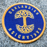 Iron-On Patch - Oaklandish Circle, Royal Blue & Gold on asphalt.