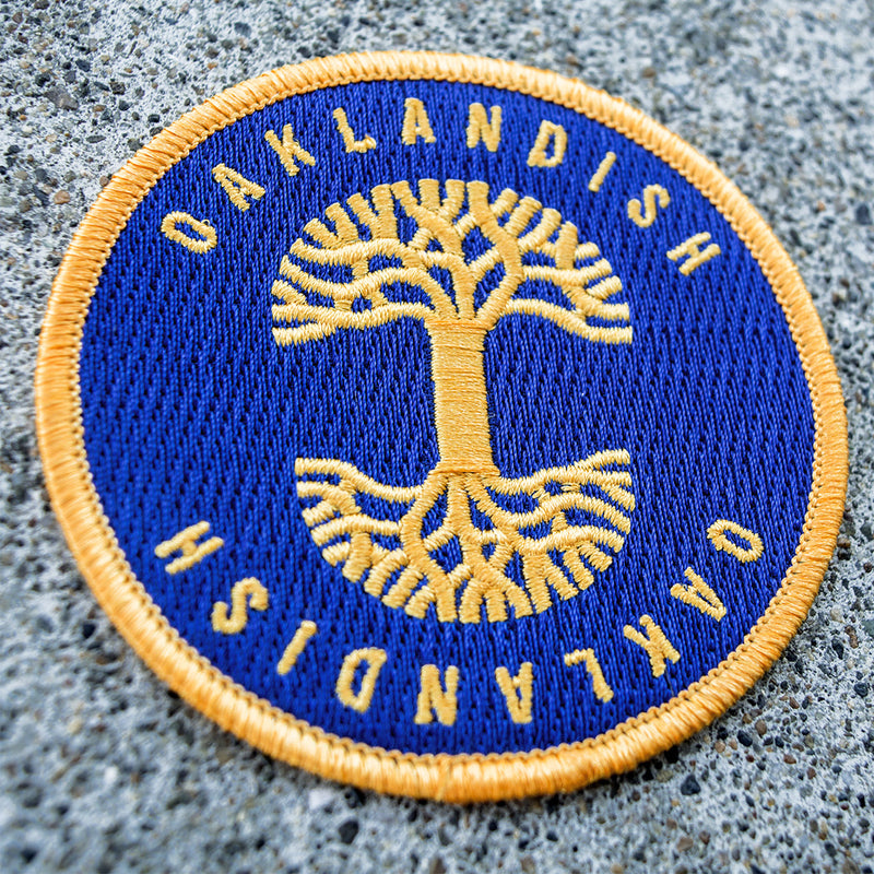 Iron-On Patch - Oaklandish Circle, Royal Blue & Gold on asphalt.