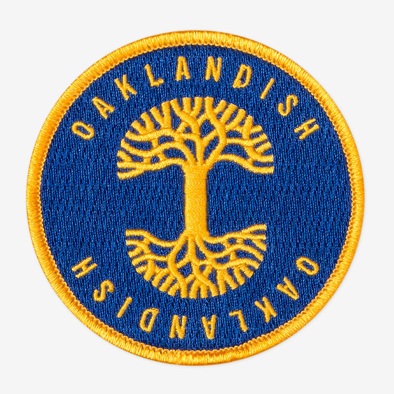 Round royal blue circle patch with embroidered gold Oaklandish tree logo in the center and Oaklandish wordmarks above and below.