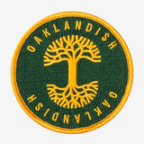 Round green circle patch with embroidered yellow Oaklandish tree logo in the center and Oaklandish wordmarks above and below.