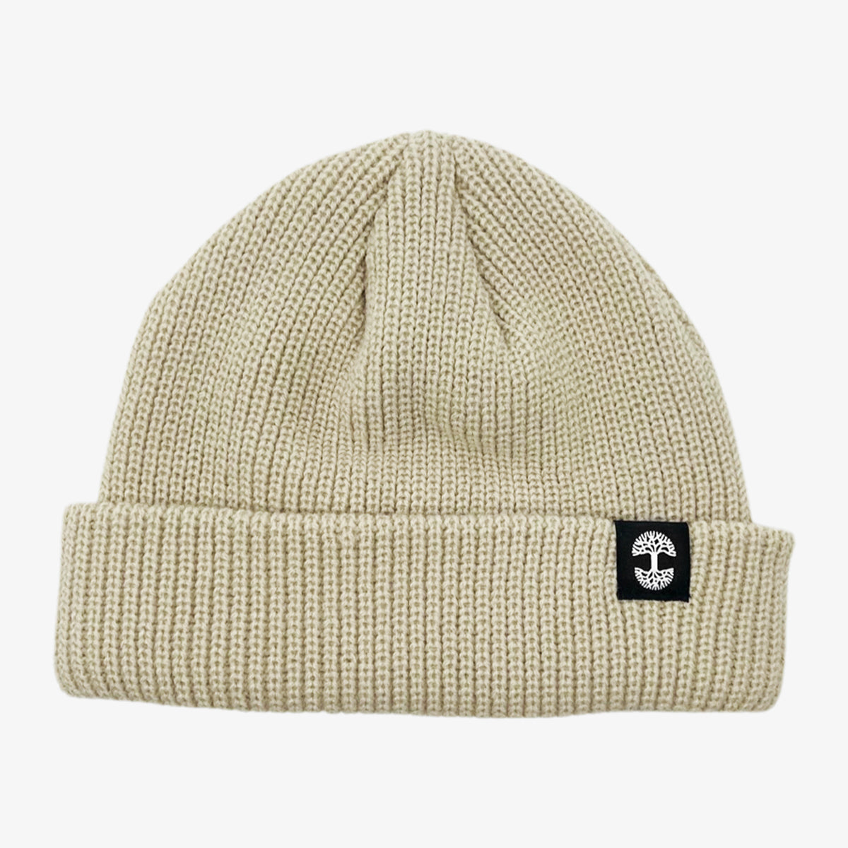 Shallow fit cream cuffed beanie with black and white Oaklandish tree logo tag on the left wear side.