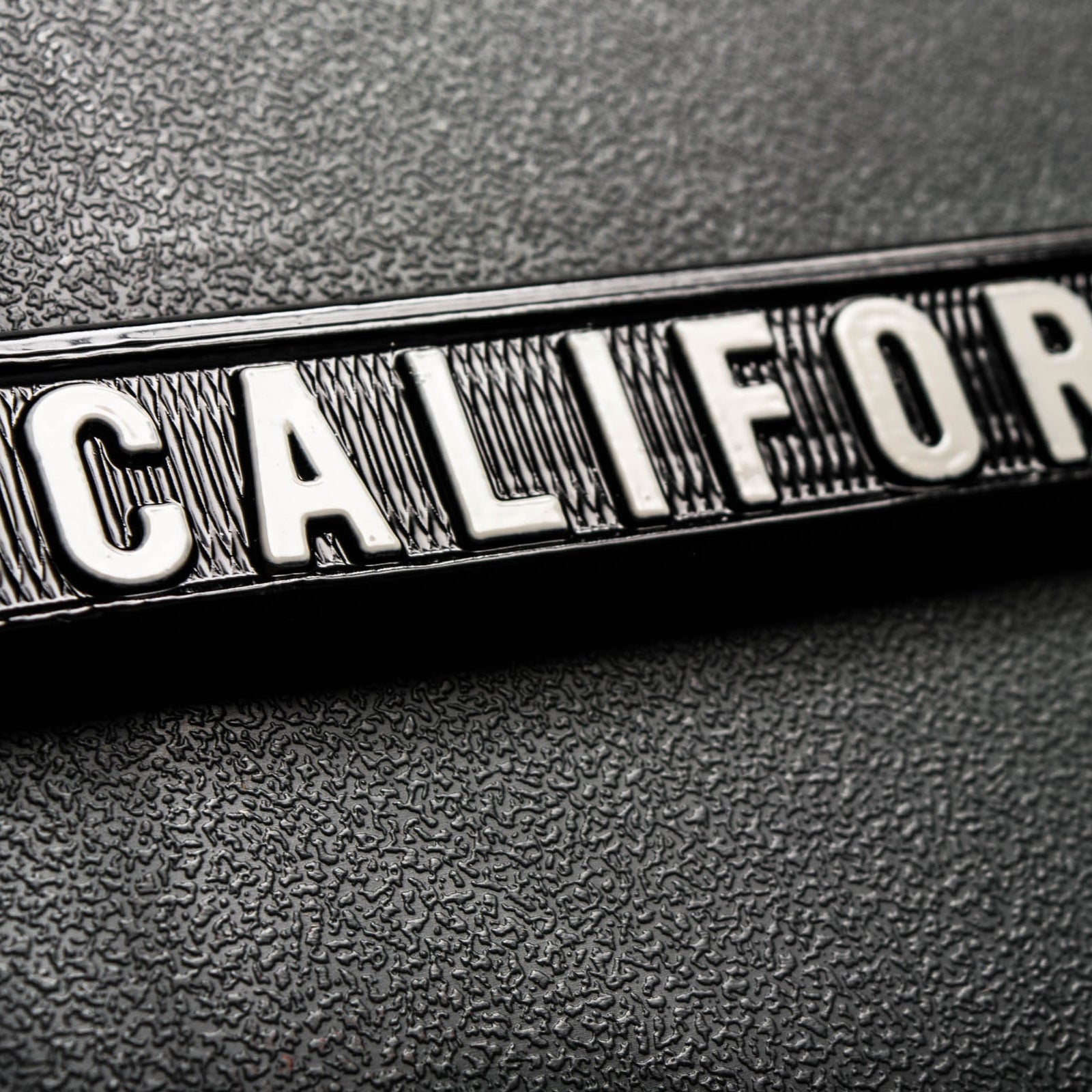 Close-up of California wordmark on a black rim of a silver license plate holder.