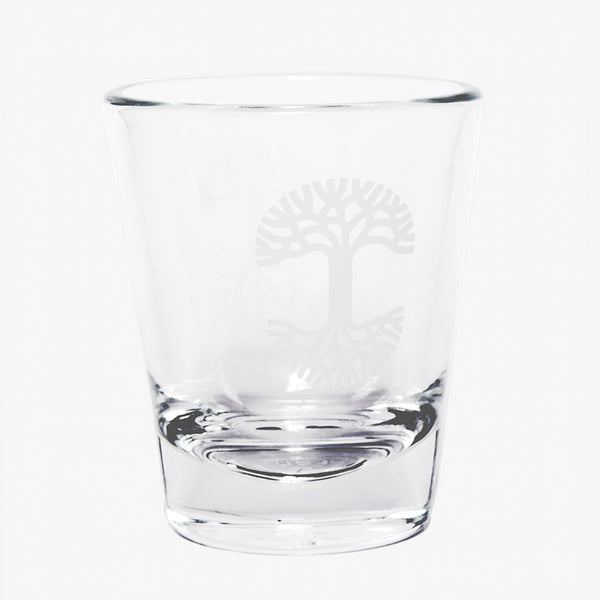 Clear glass liquor shot glass with translucent Oaklandish tree logo on the side.