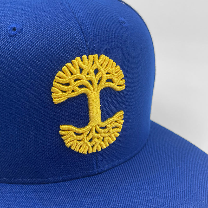 Close-up of gold embroidered Oaklandish tree logo on a royal blue cap.