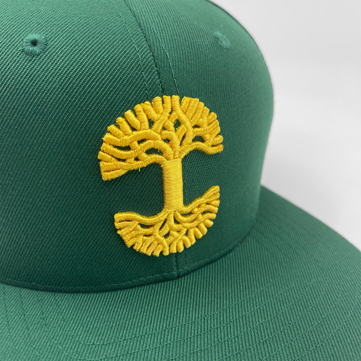 Close-up of gold embroidered Oaklandish tree logo on forest green cap.
