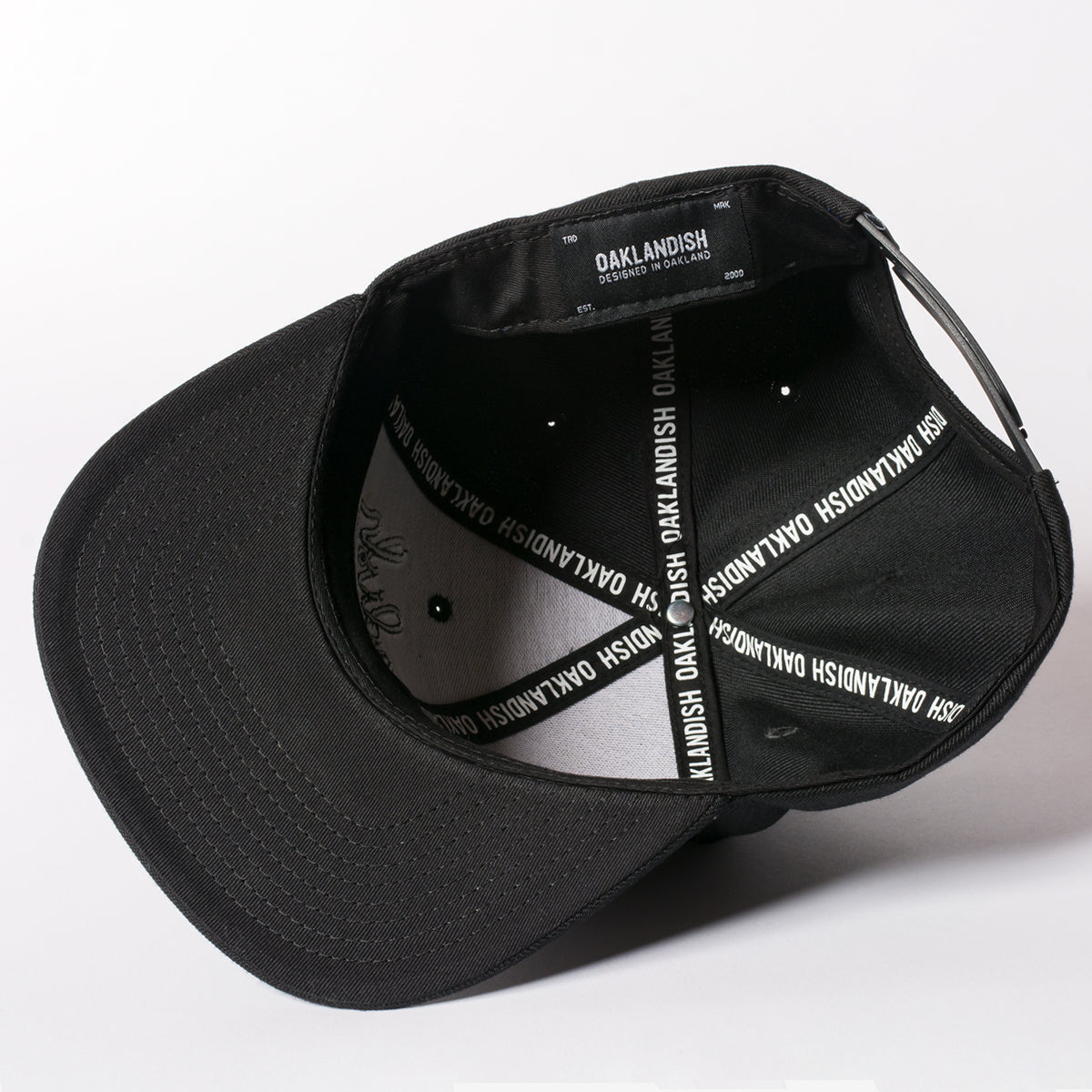 The underside of a black Oaklandish cap with Oaklandish wordmarks on the taping and Oaklandish tag. 