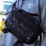 A man’s chest with wearing a cross body black hip bag with a Oaklandish wordmark and tree logo.