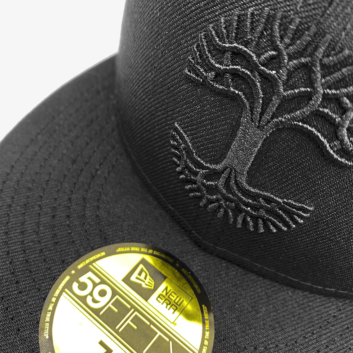 Close up of black embroidered Oaklandish logo on a black, fitted New Era cap with a black bill and gold New Era sticker. 