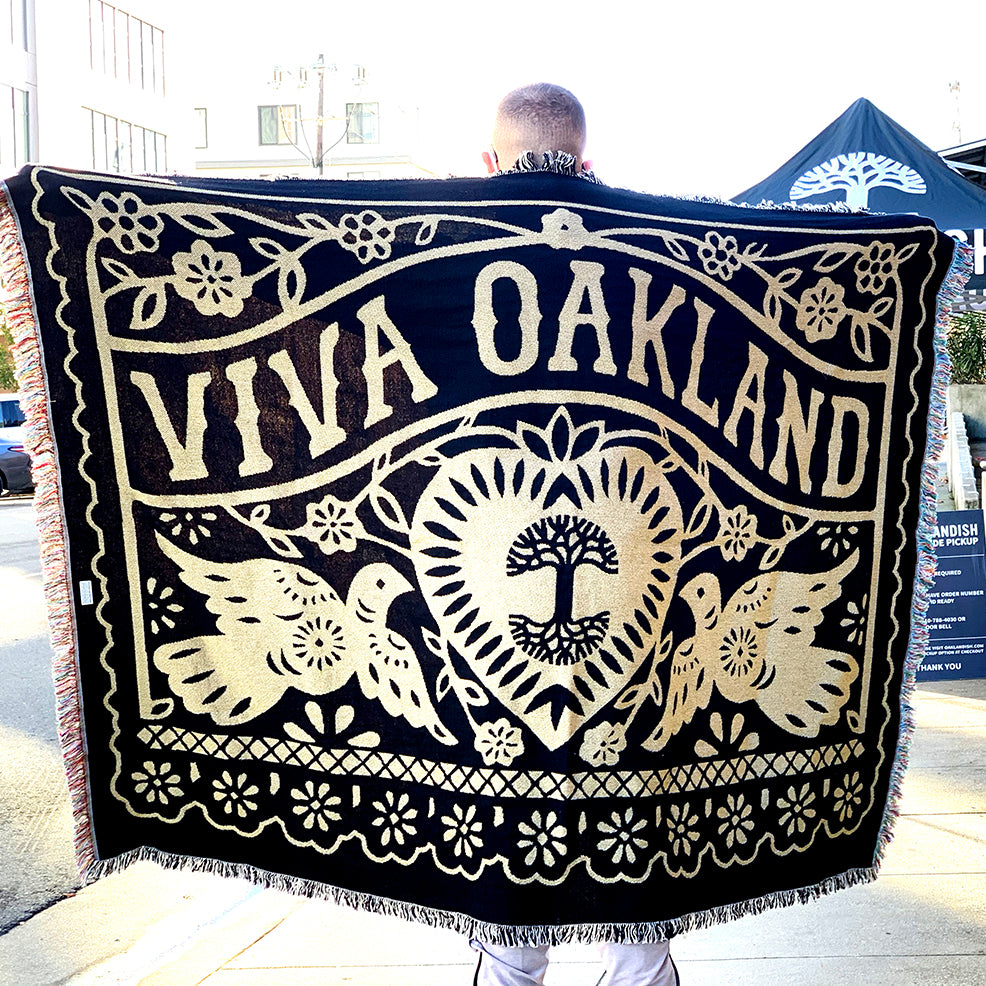 Male model with arms stretched holding throw blanket - viva oakland - black and gold -100% cotton