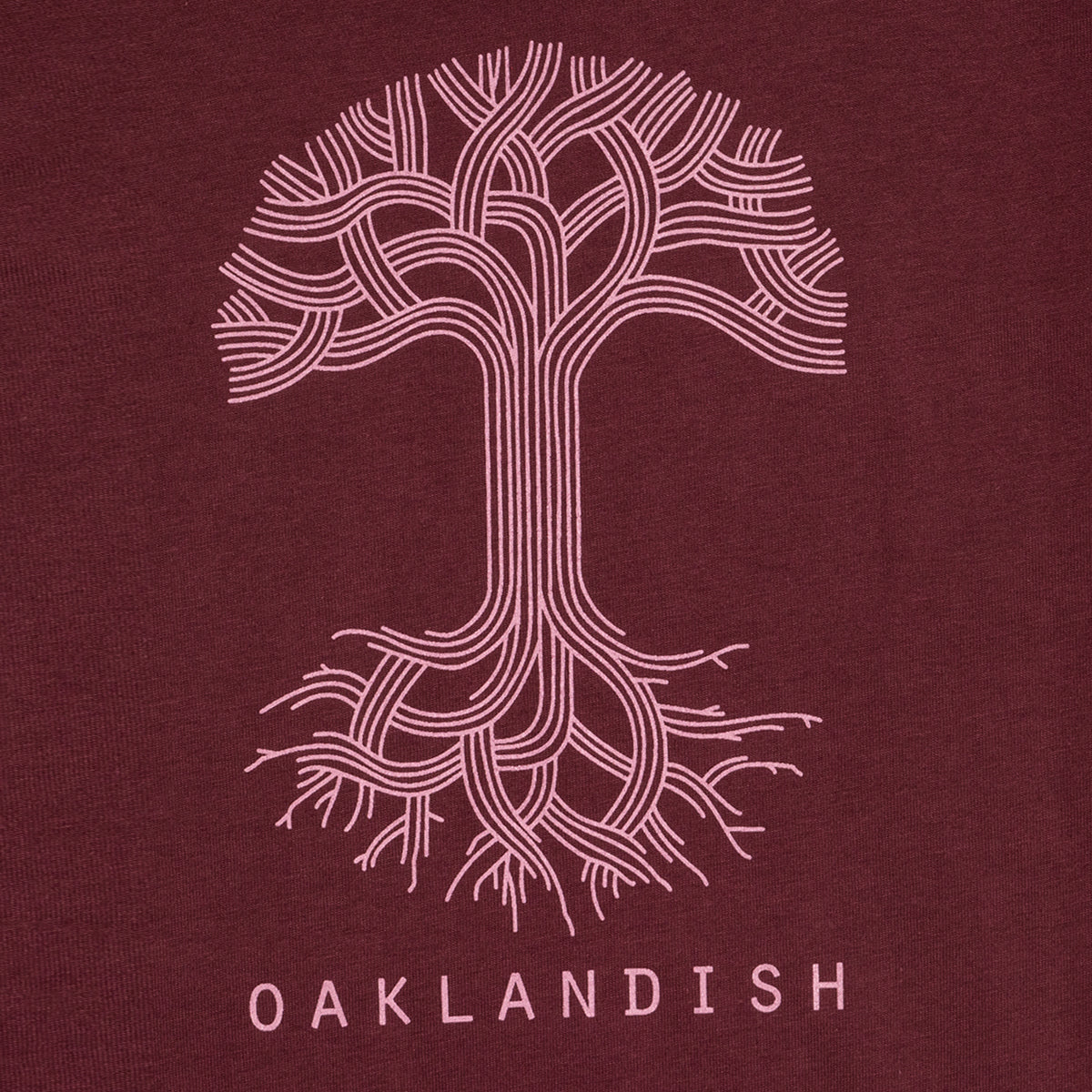 Close-up of pink classic Oaklandish tree logo and wordmark on chest of a burgundy women’s cut t-shirt.