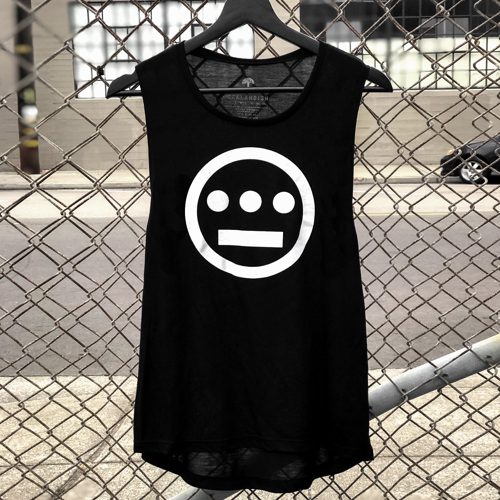 Women's black tank top with white Hiero Hip Hop Crew Classic Logo on chest hanging outdoors on a chain-link fence.