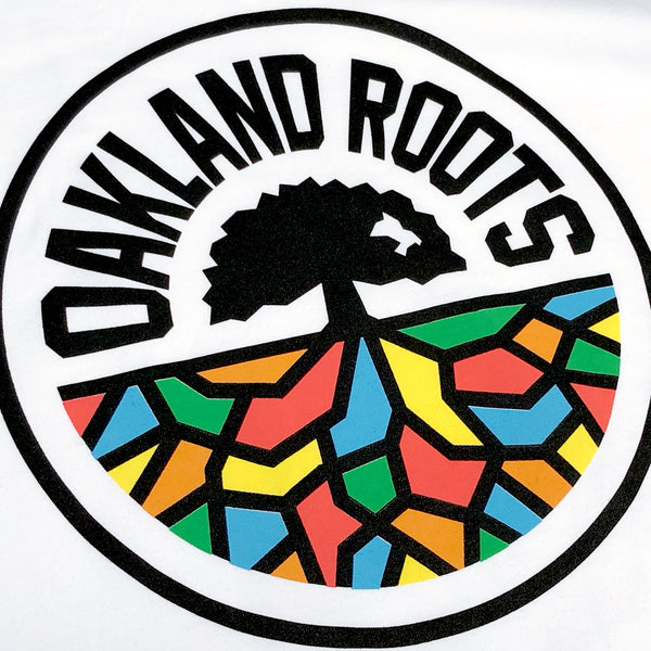 Close-up of full-color Oakland Roots circle logo on the chest of a women’s white tank top.