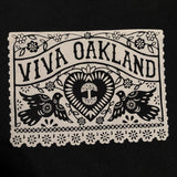 Close-up of gold Viva Oakland graphic with hearts and birds on the chest of a black women’s cut t-shirt.