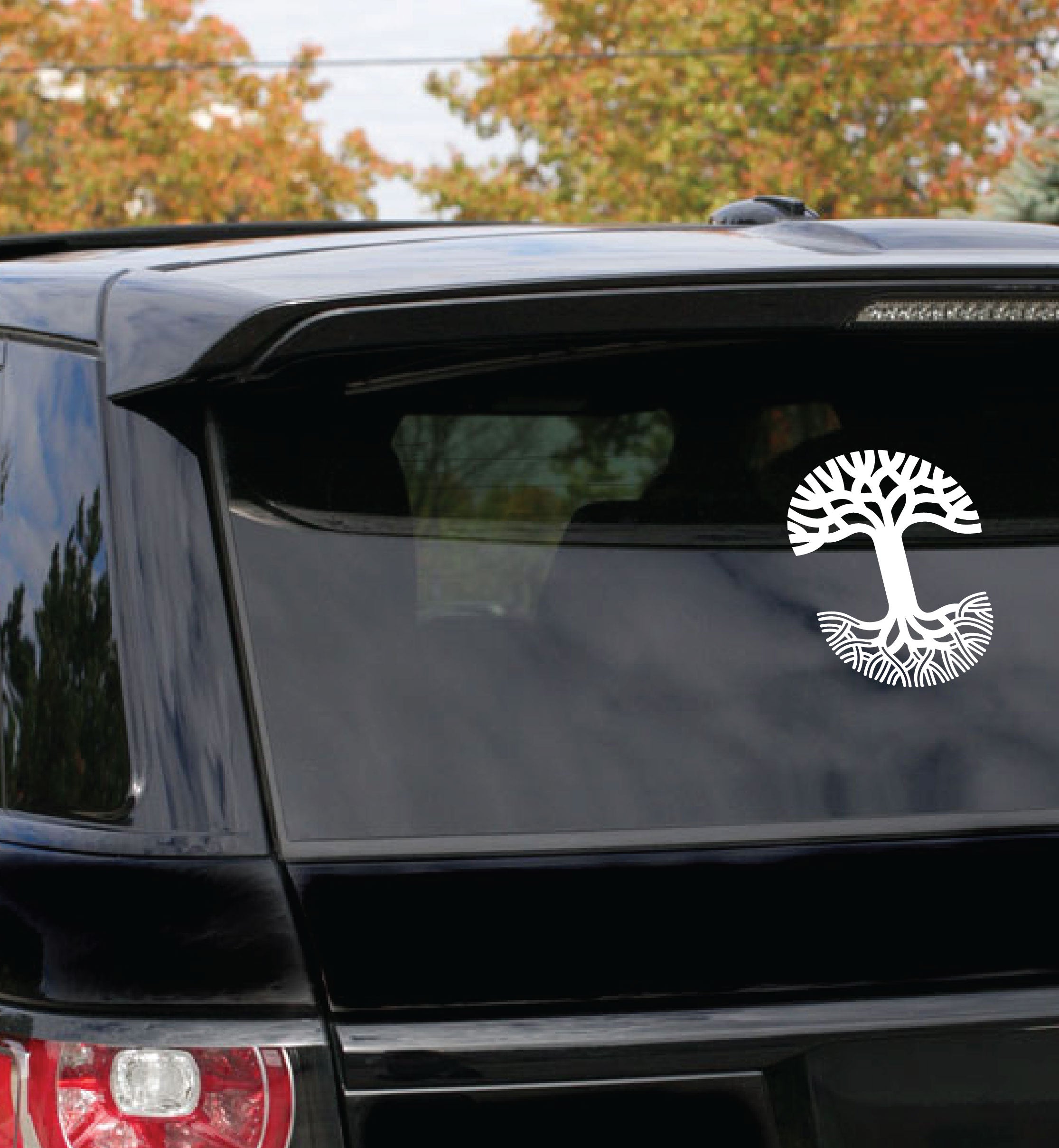 Extra large-sized white Oaklandish tree logo car window decal on the back window of a black SUV car. 